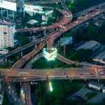 Dynamic aerial view of a bustling Bangkok expressway intersection with city lights.