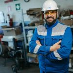 Smiling worker in blue uniform and hard hat standing in a factory setting in Russia.