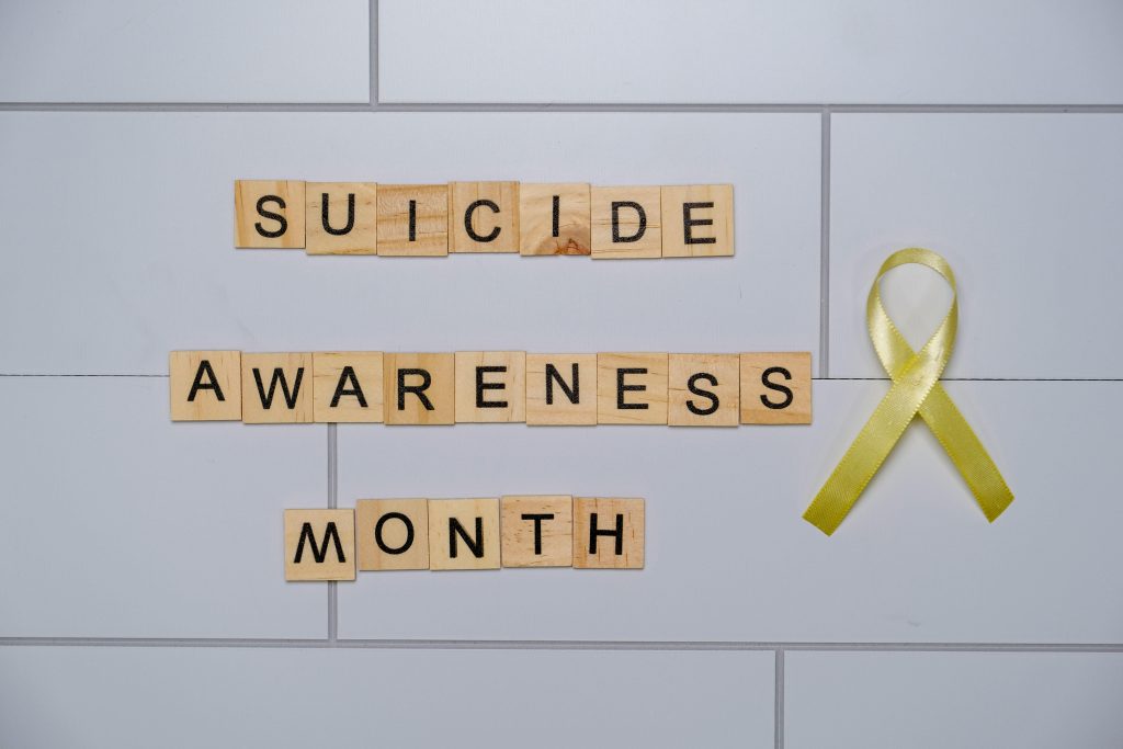 Wooden blocks spelling 'Suicide Awareness Month' with a yellow ribbon.