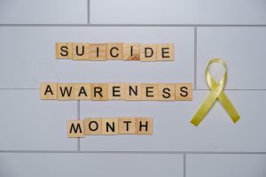 Wooden blocks spelling 'Suicide Awareness Month' with a yellow ribbon.